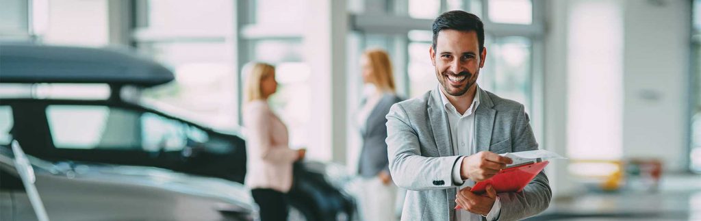 Smiling businessman shaking hands in a modern office with colleagues blurred in the background.