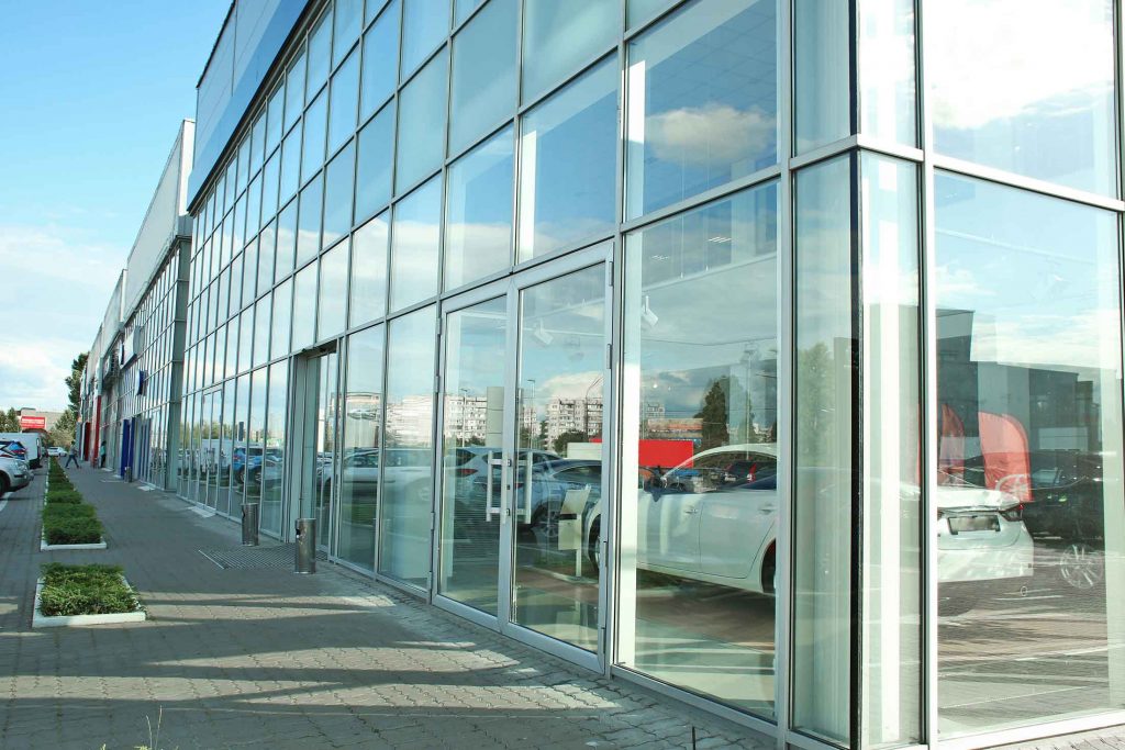 Reflective glass building facade showing cars and sky.