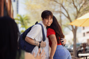 Two friends hugging outdoors, one wearing backpack
