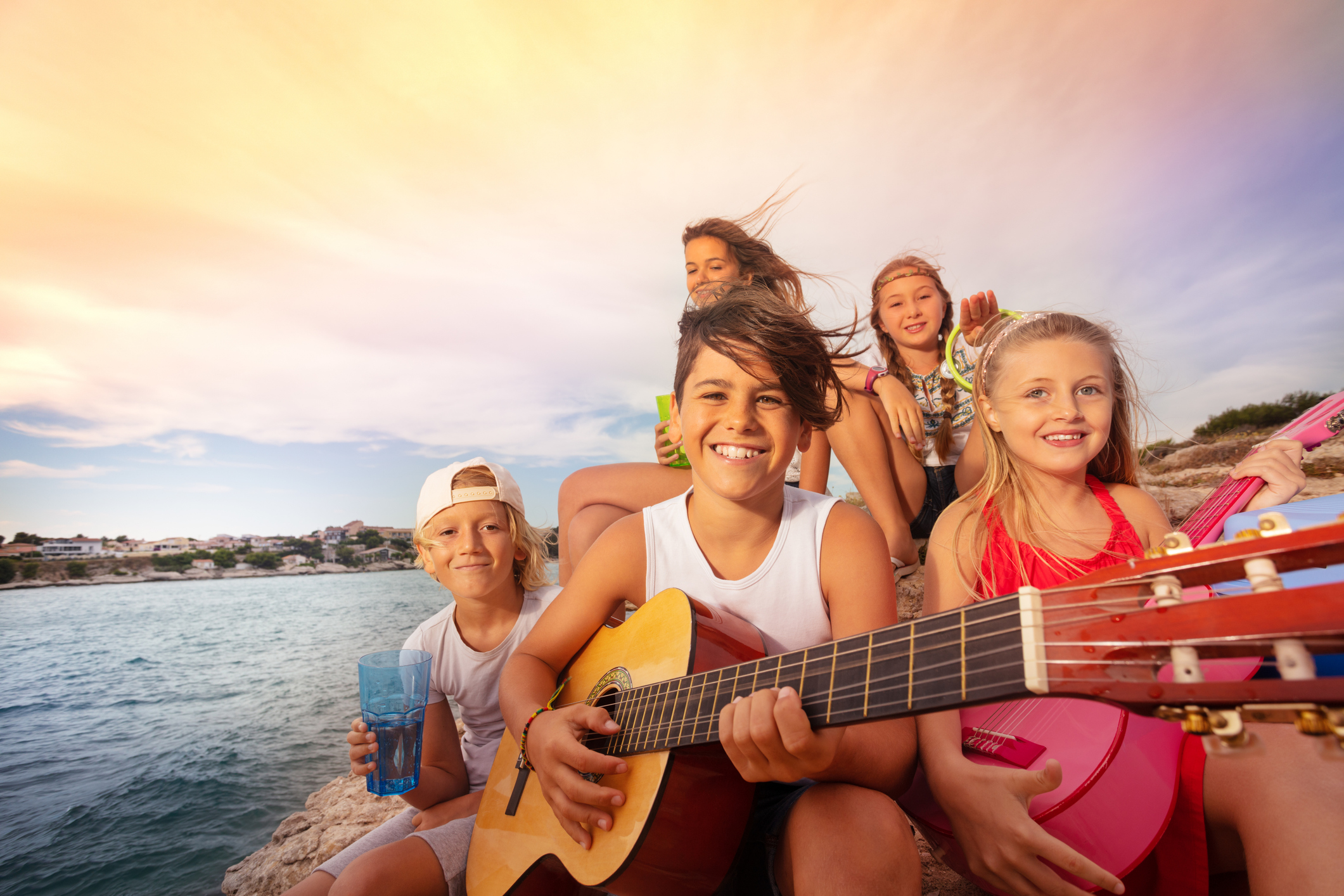 Smiling kids playing guitar by seaside sunset
