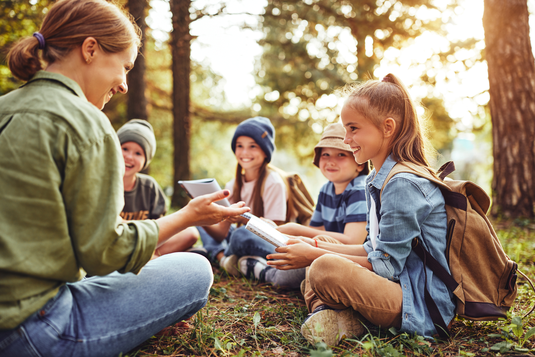 Children with backpacks reading outdoors in forest