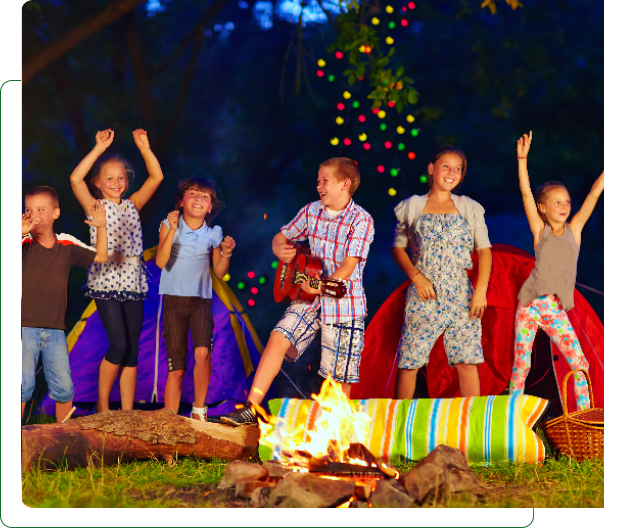 Children dancing around campfire with guitar and tents